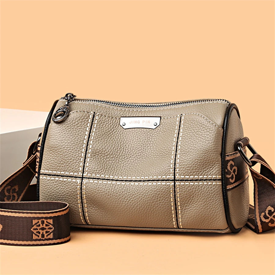 A beige luxury cowhide shoulder bag with stitching and a leather strap is displayed on a light background.