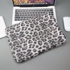 Ein Leopardenmuster-Laptop-Sleeve liegt auf einer grauen Oberfläche neben einem Laptop.