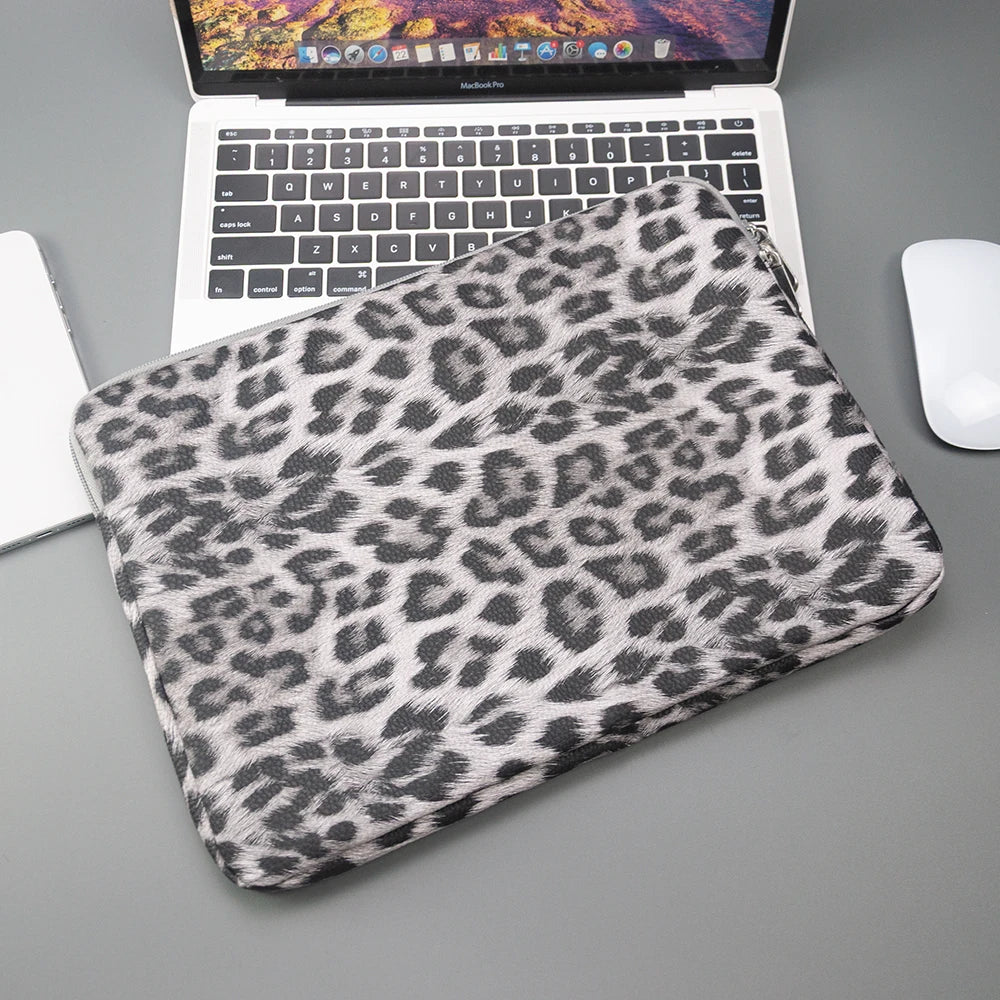 Ein Leopardenmuster-Laptop-Sleeve liegt auf einer grauen Oberfläche neben einem Laptop.