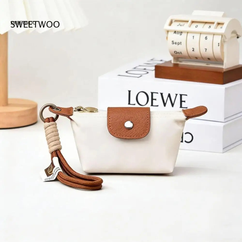 A cream-colored compact coin purse with a brown leather flap and braided strap resting on a white surface.
