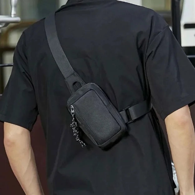 Ein Mann trägt ein schwarzes T-Shirt mit einer schwarzen Umhängetasche, die an seinem Shirt befestigt ist.