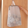 A white honeycomb mesh laundry bag is hanging on a wooden door with a hook.