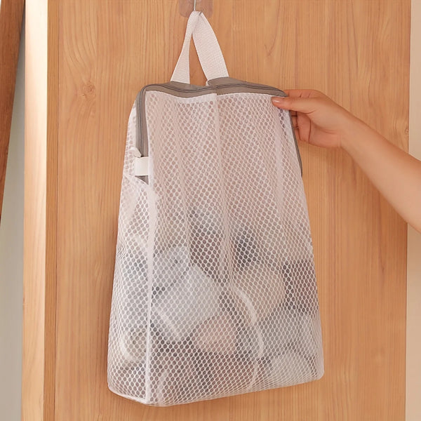A white honeycomb mesh laundry bag is hanging on a wooden door with a hook.