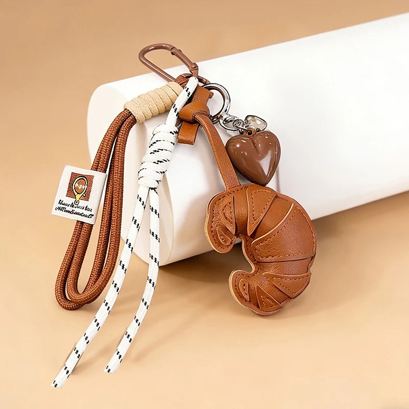 A brown leather croissant shaped keychain with a heart pendant attached to a white lanyard.