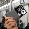 A hand holds a black RFID blocking card with an NFC symbol, being displayed in a public transit setting.