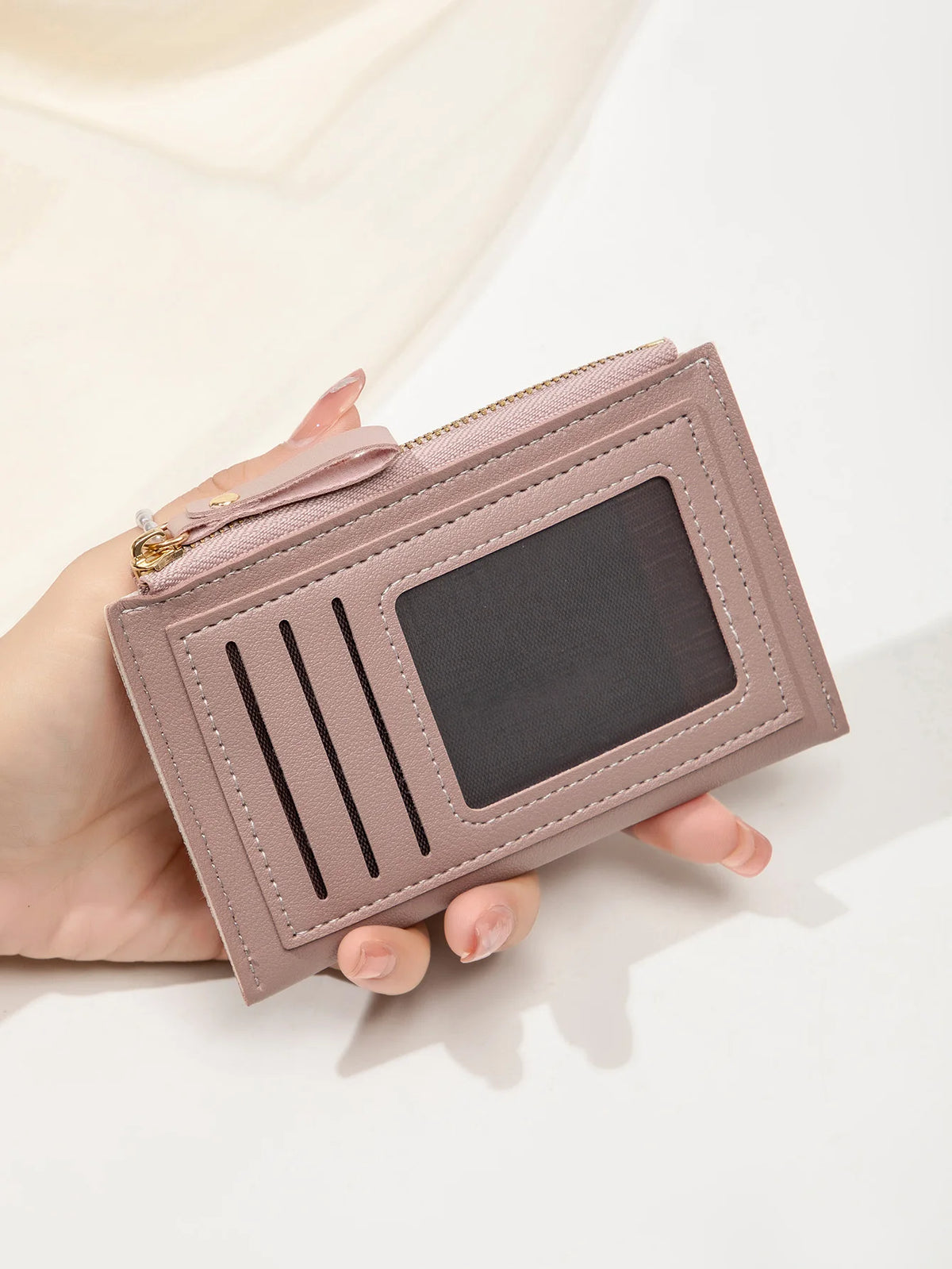 Une main tient un portefeuille en cuir PU mauve clair minimaliste avec fermeture zippée et une fente rectangulaire.