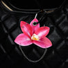 A pink and white orchid flower keychain attached to a black leather handbag.