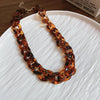 A necklace made of interlocking, amber-colored, organic cones is displayed on a white plate.