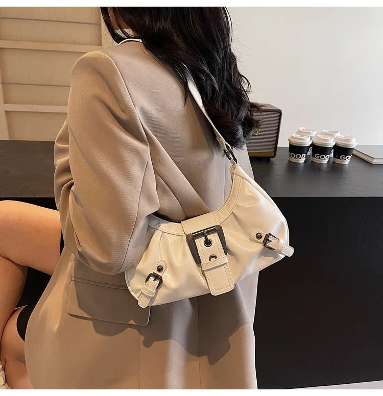 Eine Frau hält ein beiges Sakko und eine weiße Leder-Schultertasche in einem Studio.