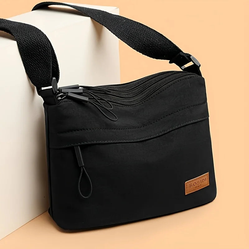 Black nylon crossbody shoulder bag with multiple zippered compartments resting on a light background.