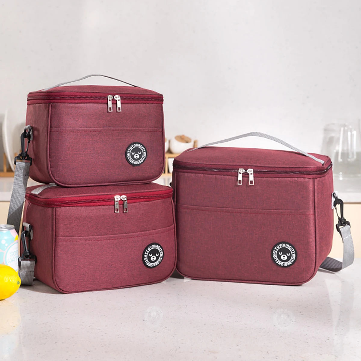 Two maroon insulated lunch tote bags with silver zippers and adjustable straps resting on a white surface.