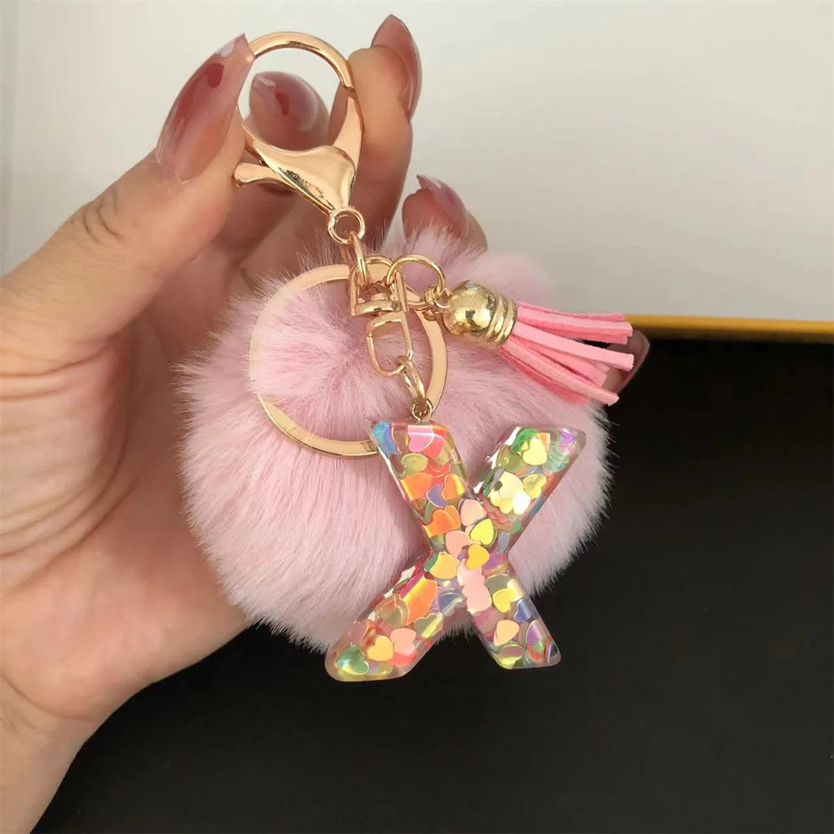 A hand holds a custom initial letter keychain featuring a shiny resin pendant and pink alphabet charm.