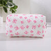 Bolsa de maquillaje blanca con estampado de lazo rosa, sobre una superficie blanca.