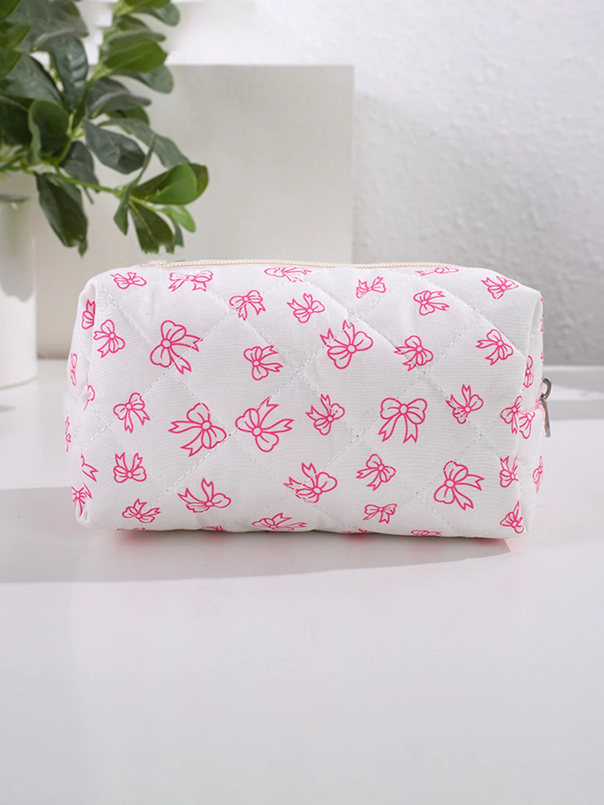 Bolsa de maquillaje blanca con estampado de lazo rosa, sobre una superficie blanca.