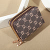 A dark brown patterned zippered card holder wallet with gold accents resting on a light beige surface.