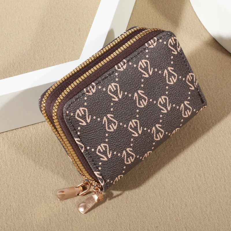 A dark brown patterned zippered card holder wallet with gold accents resting on a light beige surface.