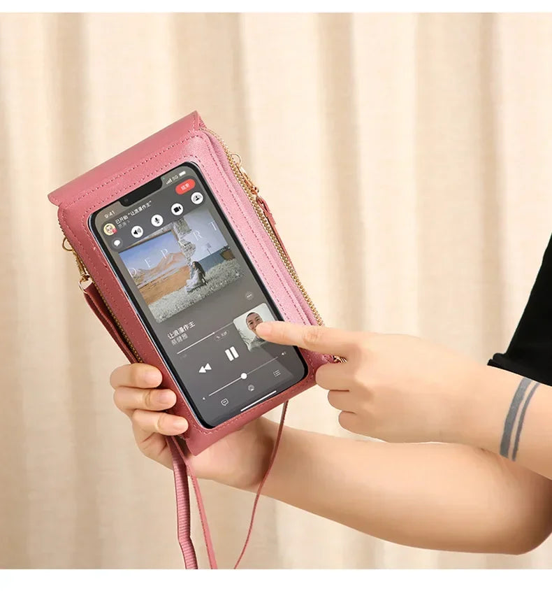 A hand holds a pink women's touch screen crossbody shoulder bag displaying a smartphone screen.