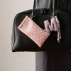 A pink polka dot eyeglass pouch with a purple initial keychain hanging from a black handbag.