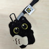 A black cat plush keychain charm with yellow eyes and a white paw, attached to a black cord.