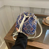A close-up of a blue and white floral patterned drawstring bucket bag with light beige straps resting on a wooden surface.