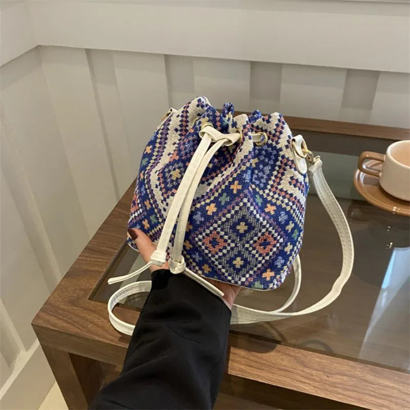A close-up of a blue and white floral patterned drawstring bucket bag with light beige straps resting on a wooden surface.