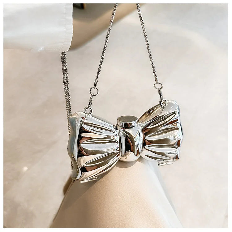 Silver elegant bowknot evening bag with a detachable chain strap displayed against a light background.