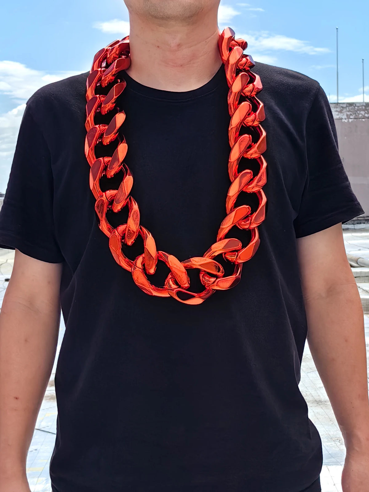 A man wearing a chunky gold acrylic Cuban link necklace with an orange-red color against a black t-shirt.