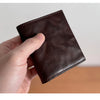 A hand holds a dark brown genuine leather bifold wallet for men.