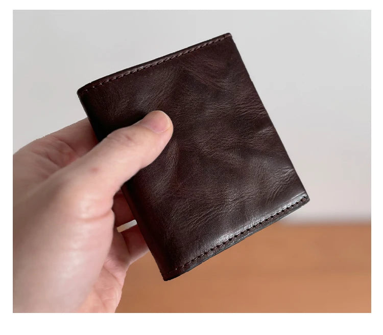 A hand holds a dark brown genuine leather bifold wallet for men.