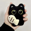Un dije de gato negro de peluche es sostenido en la mano de una persona contra un fondo claro.