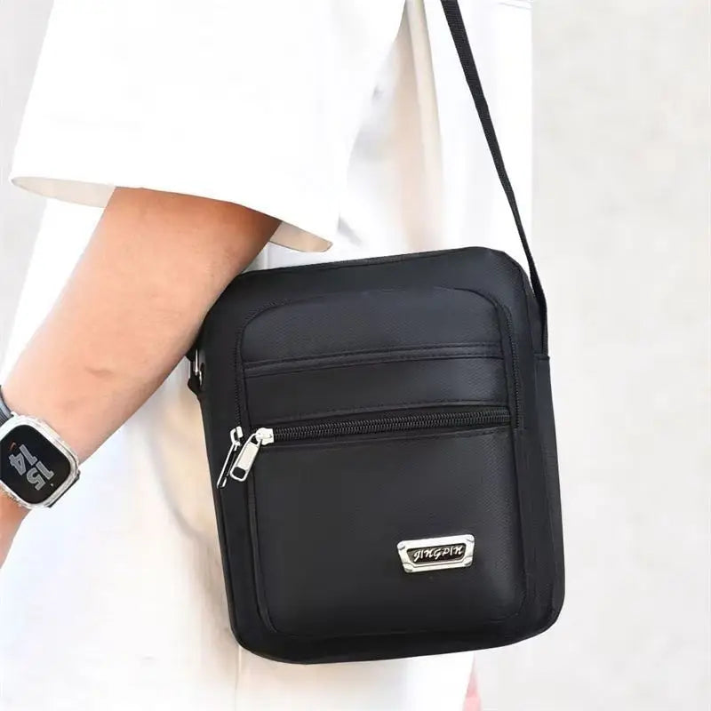 Sac de poitrine extérieur noir unisexe multicouche avec fermeture éclair et logo argenté sur un t-shirt blanc.