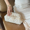 A hand places a white beaded chain shoulder clutch bag on a brown leather sofa.