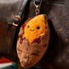A fluffy orange roasted sweet potato plush keychain hanging from a leather bag.