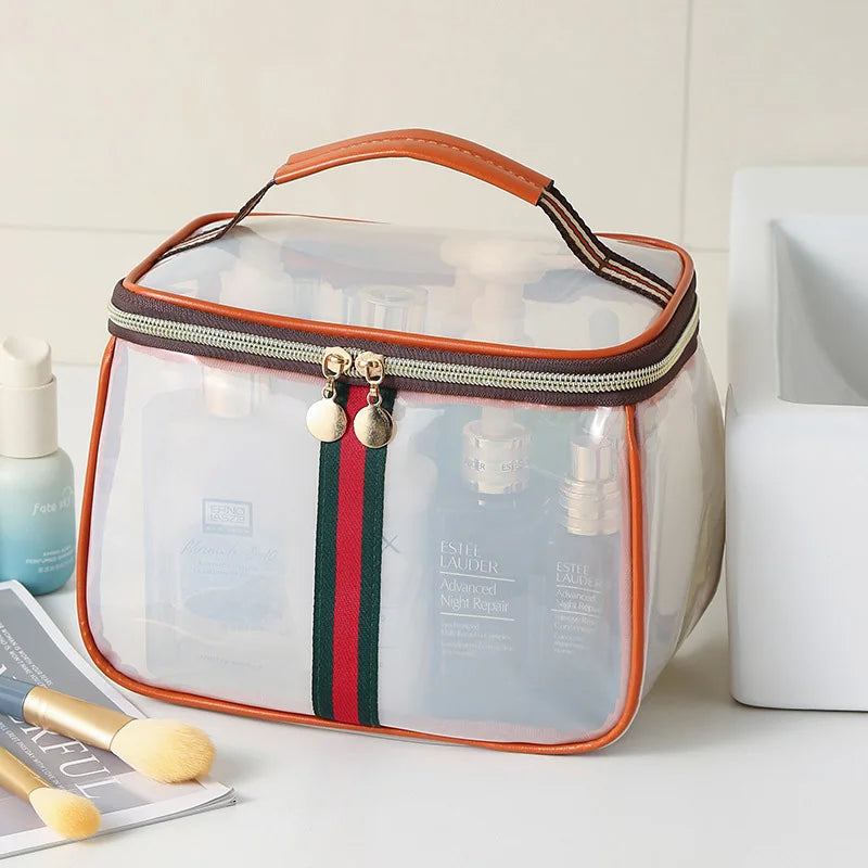 A clear cosmetic bag with an orange handle and striped fabric, containing glass bottles and brushes.
