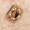 A beige leather card holder with a gold chain and a strand of light beige and tan wooden beads.