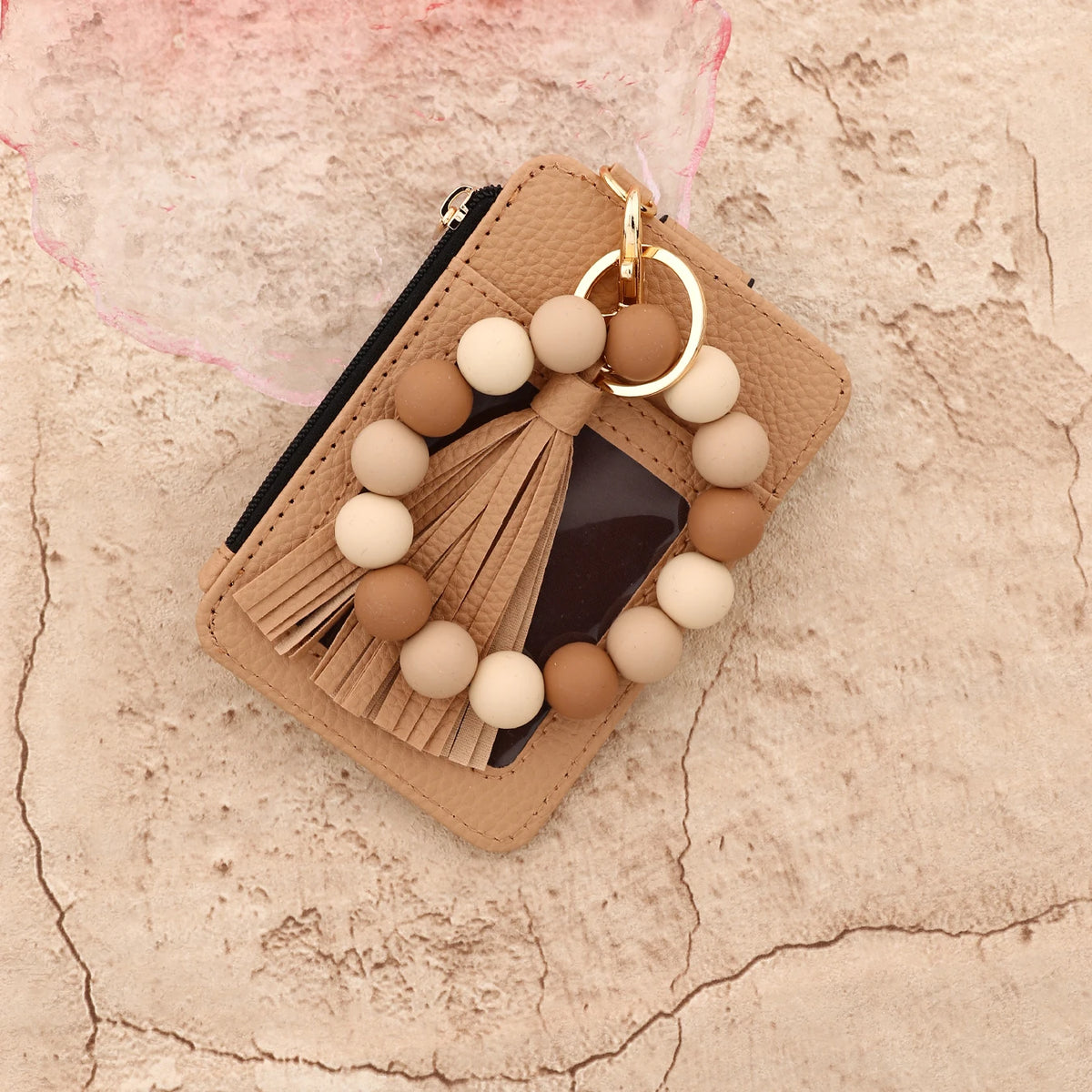 A beige leather card holder with a gold chain and a strand of light beige and tan wooden beads.