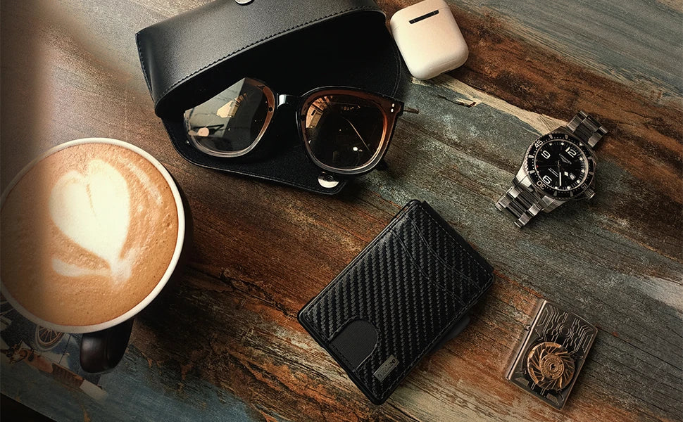 A close-up shot of a black slim minimalist men's wallet with RFID protection resting on a wooden surface next to sunglasses a