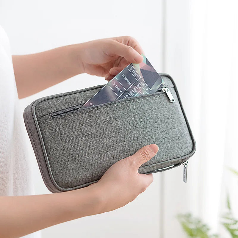 A hand is opening a gray multi-pocket waterproof travel document organizer to retrieve a card.
