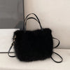 A black plush faux fur tote bag with thin black leather straps resting on a white surface.