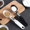 A precision digital kitchen scale is shown measuring white powder and whole seeds on a wooden cutting board.
