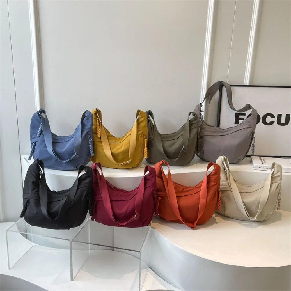 A display of various canvas crossbody bags in shades of blue, yellow, olive green, gray, maroon, orange, and beige.