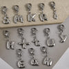 A collection of stainless steel alphabet letter charms with lobster clasps arranged on a light surface.