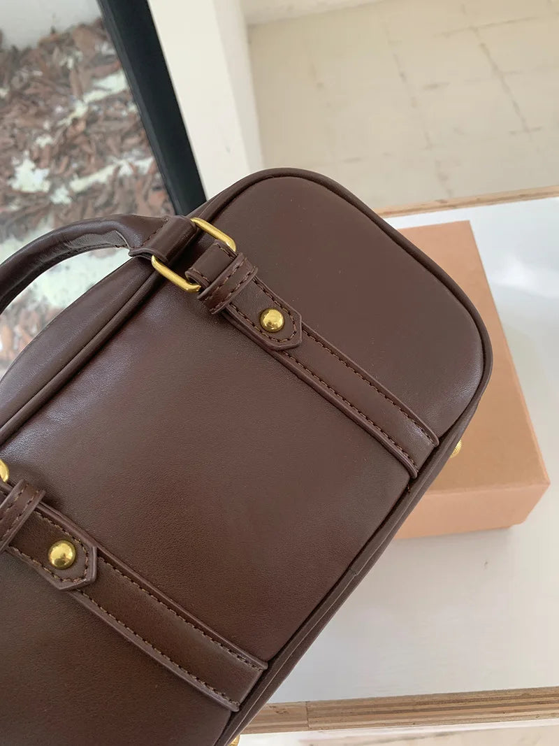 A brown vintage PU leather shoulder bag is shown in a close-up view resting on a white surface.