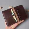 A brown genuine cowhide leather passport and ticket holder with a beige interior and stitched edges.