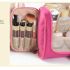 A pink multi-compartment travel pouch containing various cosmetic and grooming items like brushes and creams.