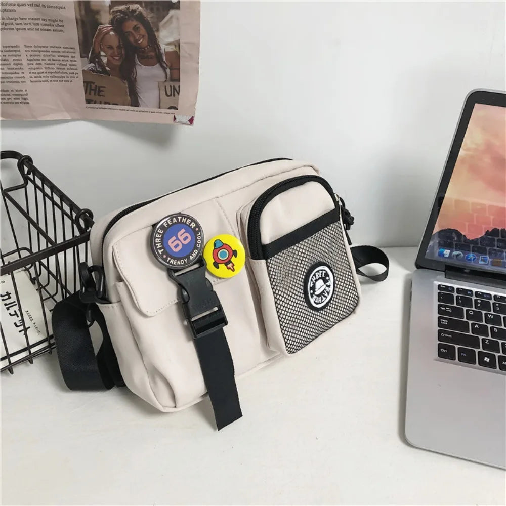 A beige canvas shoulder bag with black trim and a yellow circular charm resting on a white surface next to a silver laptop.