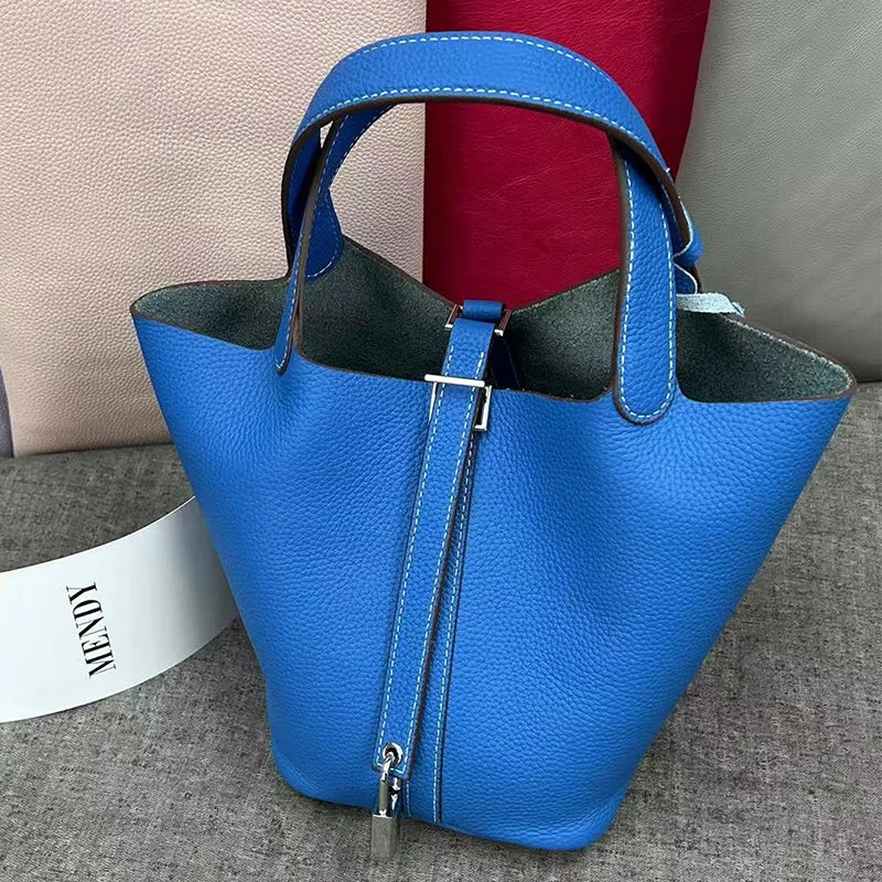 A bright blue leather bucket bag with a dark lining and silver hardware is shown on a gray surface.