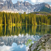 Spiegelung gezackter Berge und eines dichten Waldes in ruhigem Wasser unter blauem Himmel.