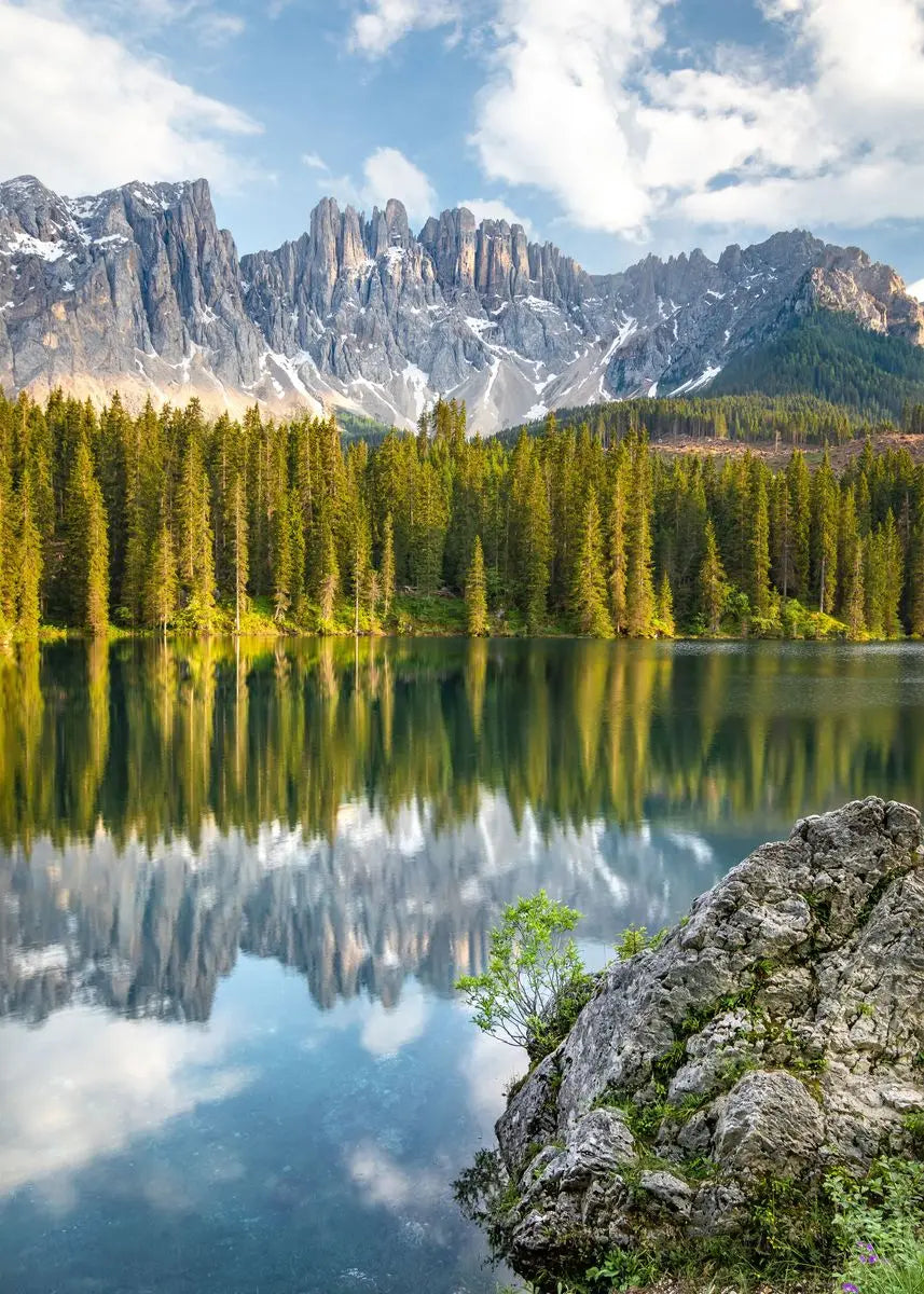Spiegelung gezackter Berge und eines dichten Waldes in ruhigem Wasser unter blauem Himmel.