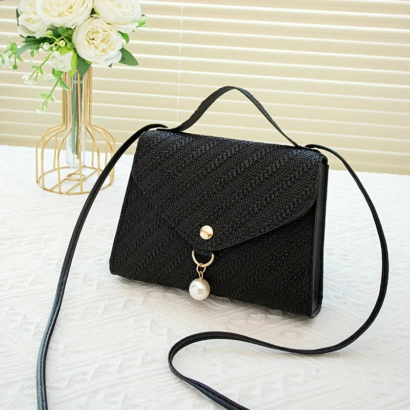 Black beaded square crossbody bag with a gold chain and adjustable black strap resting on a white surface.